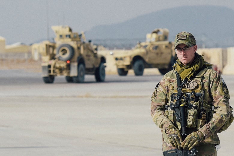 A U.S. soldier at Kandahar Air Field, with armored vehicles in the background.